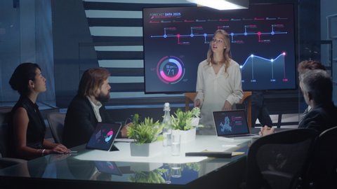 Corporate meeting room. Female executive talks to board of directors and investors using a digital interactive monitor for presentation. Screen shows charts and graphs. Shot on ARRI ALEXA Mini Camera.