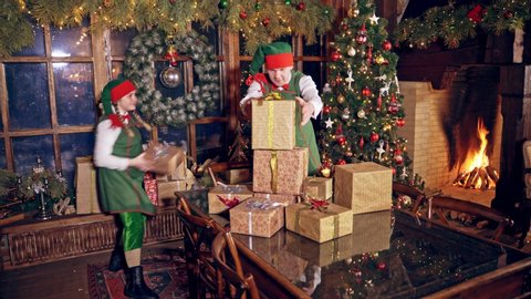 KYIV, UKRAINE - September 2019: Happy elves with many presents indoors. Christmas decorated room and elves in green costumes putting packed gifts on the table. Christmas time.