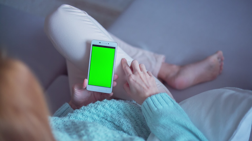 Hight quality 10bit footage of Young woman in white jeans uses SmartPhone with green screen laying on sofa at home. Made from 14bit RAW | Shutterstock HD Video #1040066150