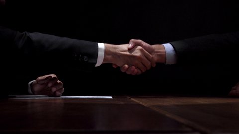 Anonymous business partners making handshake after confidential meeting in dark room 