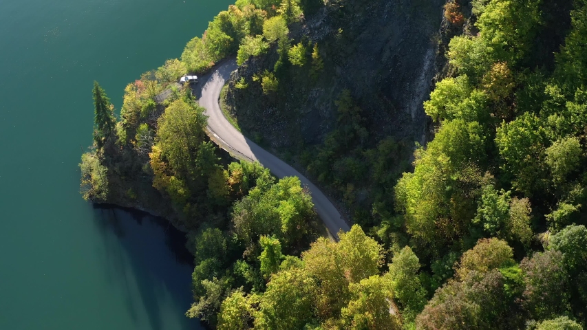Aerial shot of road in mountains near lake. Top view of sharp turn of road passing in mountains above pond.