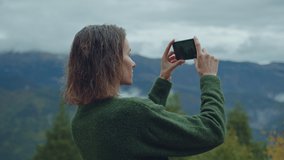 Young blogger girl with curly wet hair takes pictures or makes video on smartphone while hiking in the mountains enjoying beautiful panoramic view, Technology Connection Internet in Mountains Concept
