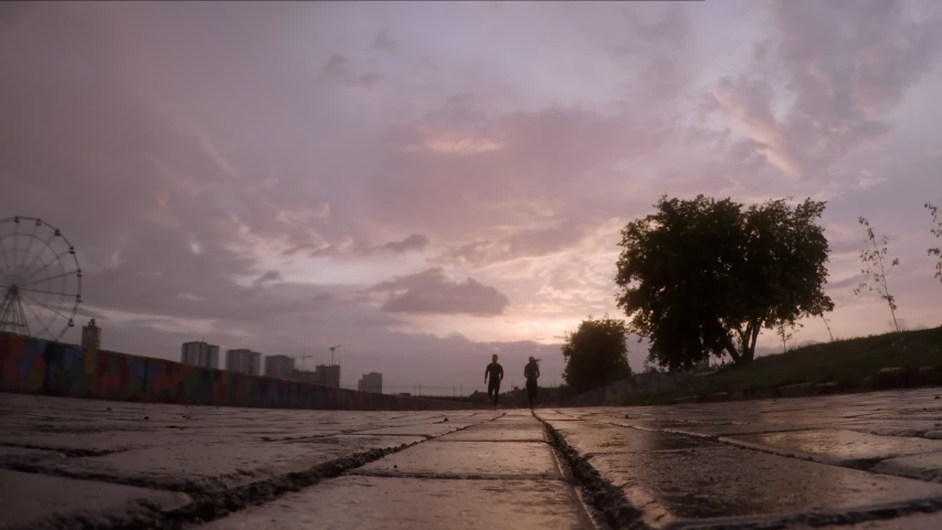 Low angle shot of silhouettes of male and female athletes running towards the camera on wet city street in the evening at sunset