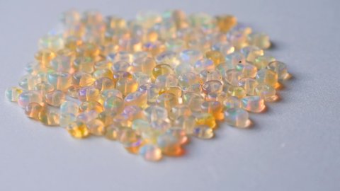 Opals gemstone from Ethiopia rotates on light background. White fire opals with rainbow like fire. Natural fire Ethiopian opal, small stones to create jewelry. Handmade stone jewelry. A pile stones.