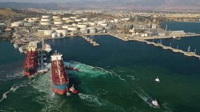 Aerial drone video of industrial bulk carrier tanker being towed by tugboats in bay and shipyard of Elefsina, Attica, Greece