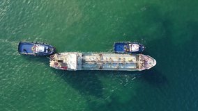 Aerial drone video of tug boats manoeuvring industrial fuel and gas carrier tanker by pushing or pulling in Mediterranean shipyard