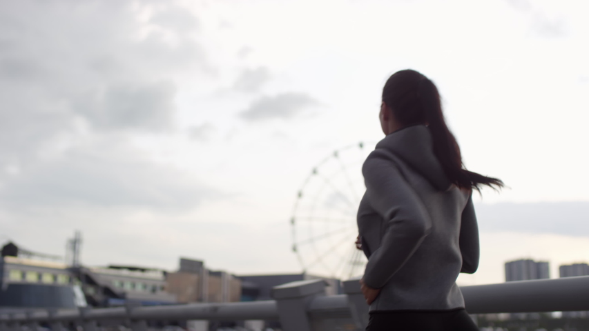 Waist up following view shot of sportive woman in hoodie running in the city while training outdoors in early morning