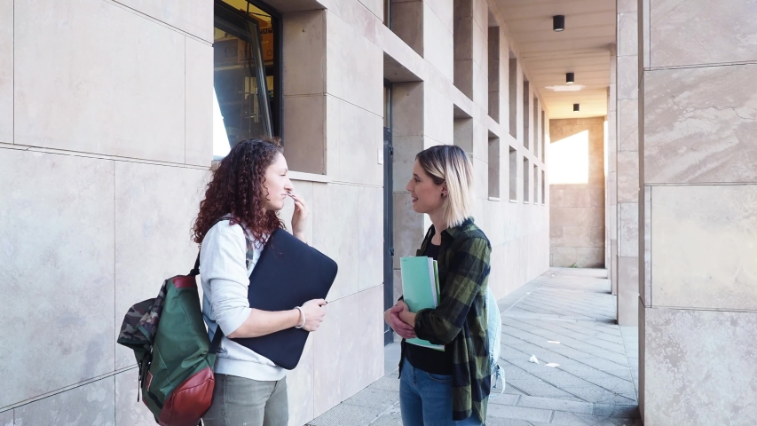 Handheld shot of female friends talking while standing on footpath in college campus