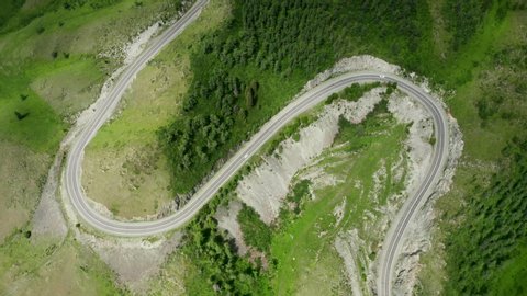 S-curve serpentine mountain road with cars in green forest of Siberia, top down aerial view. Highway R-256 Chuysky Trakt in Altai Republic, Russia