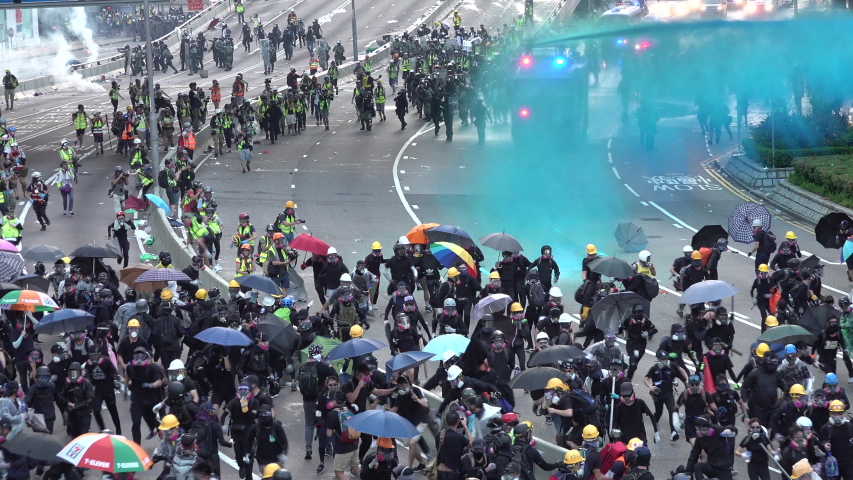 HONG KONG – 15 SEPTEMBER 2019: Crowds of protesters wearing black clothes, protective helmets and gas masks run from police, as special forces move in with water cannon and tear gas