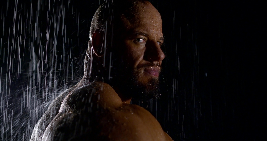 Close-up portrait of a brutal bodybuilder in the dark in the rain stands and looks at the camera. Concentrated male gaze | Shutterstock HD Video #1040112500