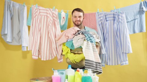 handsome funny housekeeper with basket full of clothes posing to the camera in laundry room with yellow wall. Occupation, job, profession