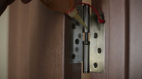 A man oiling door hinges in an apartment.
door hinge lubrication.