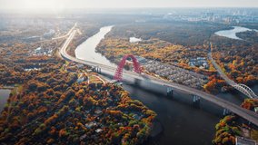 Amazing aerial panorama of red Picturesque bridge over the Moscow river. Camera moving around showing large arch of the bridge in colorful autumn landscape and its road traffic in motion timelapse.