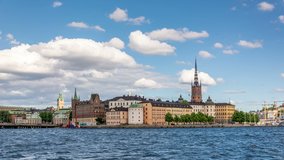 Panoramic view on Riddarholmen islet with Riddarholmen church tower, part of Gamla Stan, the old town of Stockholm, Sweden. White clouds move fast across the blue sky. Time lapse video.