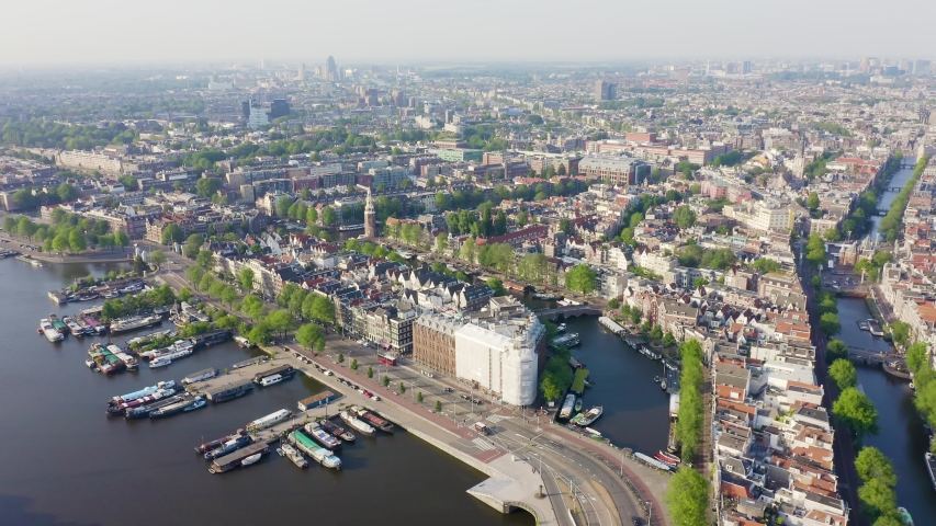 Amsterdam, Netherlands. Soaring over historic rooftops and canals towards the iconic Central Station, bathed in soft daylight. Aerial view