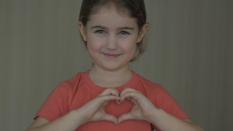 Cute little girl making a heart with her hands and smiling. Young beautiful girl smiling in love showing heart symbol and shape with hands. Romantic concept. Mothers Day. 