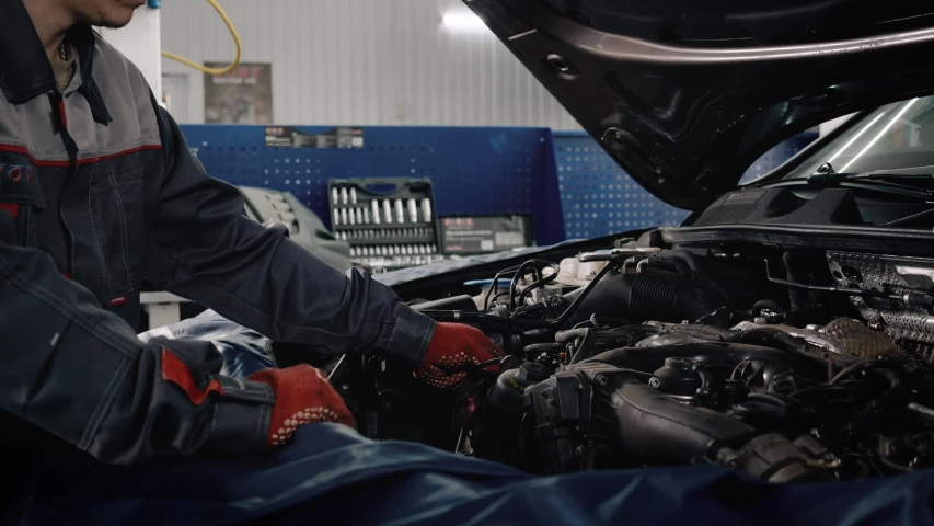 Car service, repair, maintenance and people concept - mechanic man working at workshop. Proffesional car maintenance at service station.