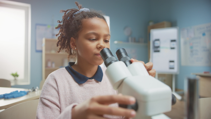 Portrait of Smart Little Schoolgirl Looking Under the Microscope. In Elementary School Classroom Cute Girl Uses Microscope. STEM (science, technology, engineering and mathematics) Education Program Royalty-Free Stock Footage #1040157164
