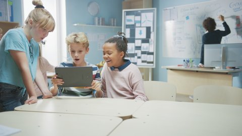 Elementary School Computer Science Class: Two Girls and A Boy Use Digital Tablet Computer with Augmented Reality Software, They’re Excited, Full of Wonder, Curiosity. Children Playing and Learning