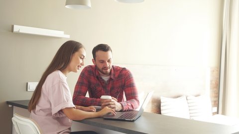 Handsome man together with beautiful young woman spending time in front of laptop computer, staring at screen with positive emotions