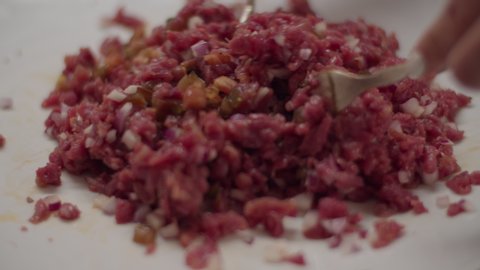 Close up of cooking meat tartare in slow motion. Mixing chopped meat with forks. 