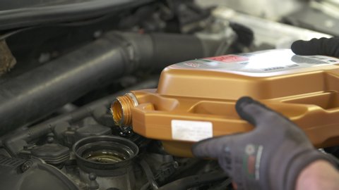 Male Mechanic Refilling Motor Oil Change Lube Change, Working Repairing An Open Engine Cover for Vehicle Inspection in a Garage Auto Shop
