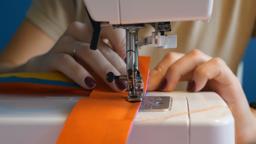 girl dressmaker concentrated stitching details orange waist bag on a sewing machine close-up, slow motion