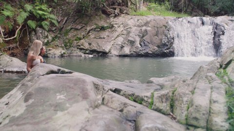 Young beautiful girls in bikinis going swimming in secluded river near waterfall. Wide shot on 4k RED camera.