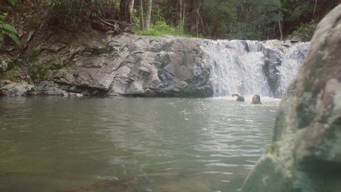 Young beautiful girls in bikinis swimming in secluded river near waterfall. Wide shot on 4k RED camera.
