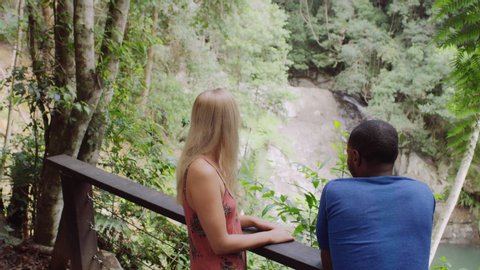 Two millennial friends laughing in front of small waterfall in an Australian rainforest by safety railing during daytime. Medium shot with camera pan around on 4k RED camera.
