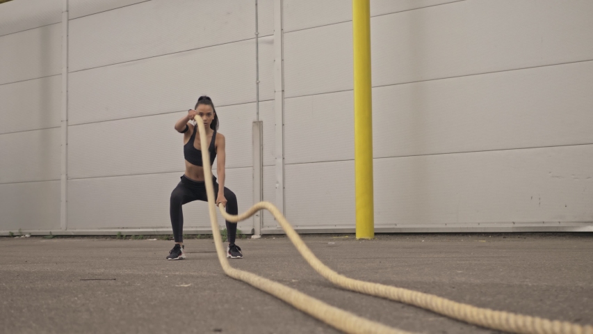 Concentrated beautiful young sporty brunette woman in black sportswear making excercise with a rope outside at the street