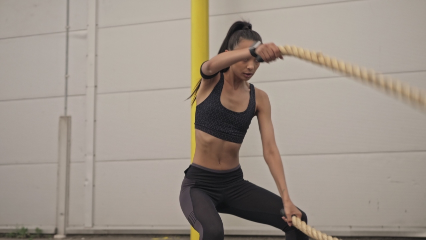 Serious beautiful young sporty brunette woman in black sportswear making excercise with a rope outside at the street