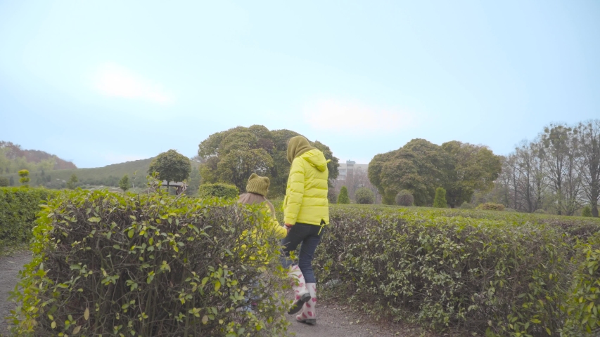 Back view of happy Caucasian daughter jumping along green bushes with her cheerful mother. Big black doberman running out from bushes and joying them. Happy family resting with their dog outdoors.