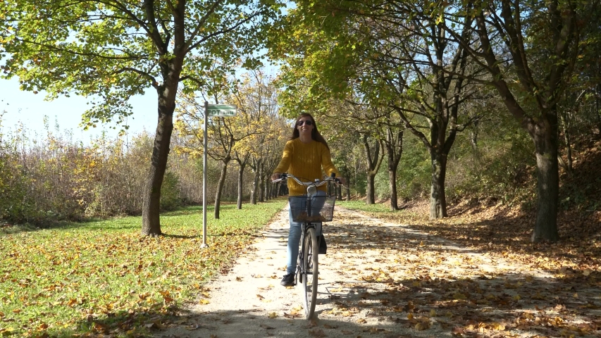 SLOW MOTION Young woman walking with classy city bicycle on a gravel path in a city park toward camera