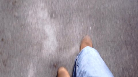 a man in brown shoes and jeans is on the asphalt road. the camera shoots footsteps