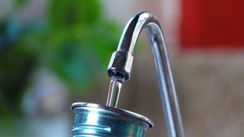 Close up person refilling reusable metal water bottle at reverse osmosis faucet in kitchen. Reusable drinking bottles are a much needed alternative to disposable plastic ones.