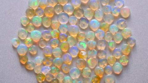 Opals gemstone from Ethiopia rotates on light background. White fire opals with rainbow like fire. Natural fire Ethiopian opal, small stones to create jewelry. Handmade stone jewelry. A pile stones.