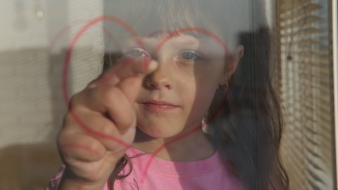 Art picture on the glass. Happy child look to the draw of a heart on the window.