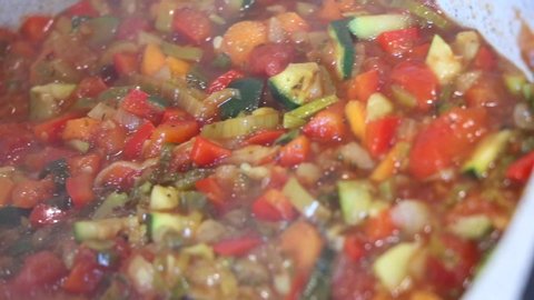 Ratatouille cooking in a white pan. Family scene : a mother is preparing lunch in a kitchen with this special french dish. Colorful with summer vegetables. Vegetarian, vegan, organic and healthy food.