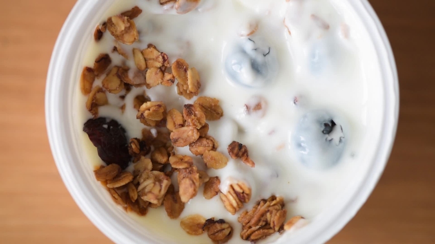 Yogurt with granola and blueberries in plastic jar. Closeup view of taking spoonful of yogurt with granola. Healthy breakfast or snack food, clean eating concept Royalty-Free Stock Footage #1040194082