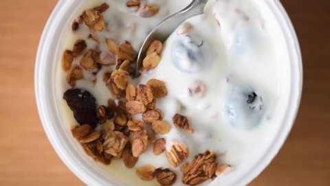Yogurt with granola and blueberries in plastic jar. Closeup view of taking spoonful of yogurt with granola. Healthy breakfast or snack food, clean eating concept