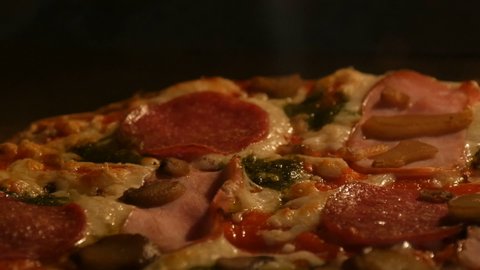 Delicious pizza with mushrooms, salami, bacon, herbs, and cheese is cooked in the oven