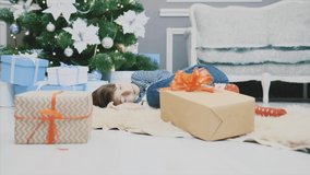 Lovely video of little boy sleeping on white carpet under christmas tree, among Christmas presenst, curling up.