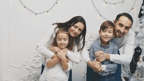 Happy family members: mother hugging daughter, father hugging son, on white background near christmas tree.