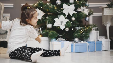 Cute little girl playing with someone, she pushes a giftbox and it comes back to her, sliding on the floor, then she makes a split exercise.