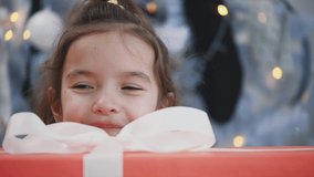 Pretty kid examines the biggest giftbox with white bow on Christmas morning.