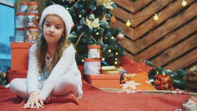 Disappointed little girl wearing Christmas costume sitting in lotos position over wooden christmas background, frowning her face.
