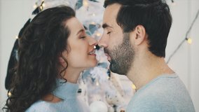 Faces of loving couple with eyes closed, touching noses over christmas background.