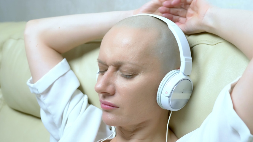 Close-up. a bald woman in headphones listens to music and moves her head to the beat of the music. | Shutterstock HD Video #1040213930